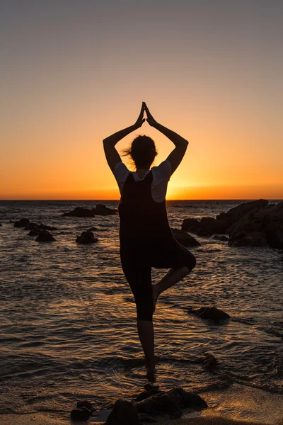 Silhouette giovane donna che pratica yoga sulla spiaggia al tramonto . — Foto Stock