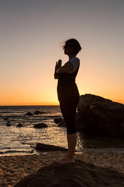 Silhouette young woman practicing yoga on the beach at sunset. — Stock Photo, Image