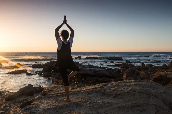 Silhouette young woman practicing yoga on the beach at sunset. — Stock Photo, Image