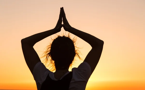 Silhouette giovane donna che pratica yoga sulla spiaggia al tramonto . — Foto Stock