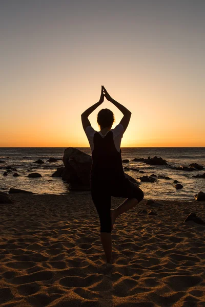 Silhouette young woman practicing yoga on the beach at sunset. — Stock Photo, Image