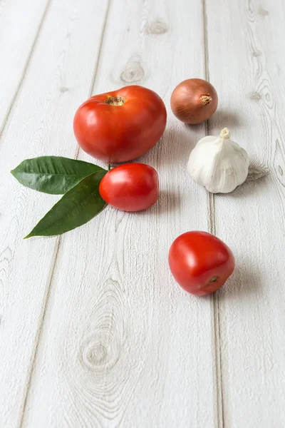 Fresh tomatoes and garlic and onion on wooden board — Stock Photo, Image