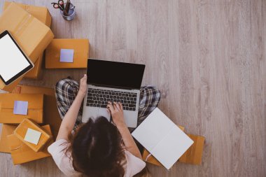 Genç bir kadın internette ürün satıyor. Defterdeki siparişleri kontrol et. Kadın küçük bir işletme sahibi. Müşterilerle irtibata geçmek için elverişli ve hızlı çalışın. İnternette fikirler satmak, küçük işletmeler