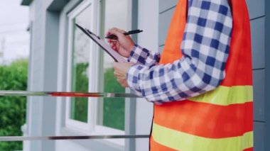 Turuncu yansıtıcı yelek giyen mühendis veya müfettişler binanın inşaat sahasındaki panolarla, müteahhit denetimleriyle ve mühendislik kavramlarıyla notlar alıp kontrol ediyorlar..