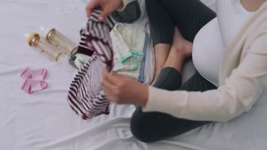 Annem yaklaşan bebeğe hazırlanmak için bebek kıyafetlerini katlıyor. Hamile bir kadın yeni doğan için kontrol ediyor. Anneler için hamilelik hazırlığı kavramı.