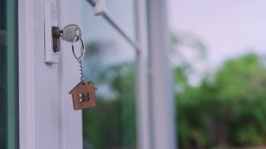 Bir evin kilidini açmak için ev sahibinin anahtarı kapıya takılı. Kira ve satış için ikinci el ev. Anahtarlık rüzgarda savruluyor. Yeni ev sahibi, kira, satış, yenileme, yatırım.