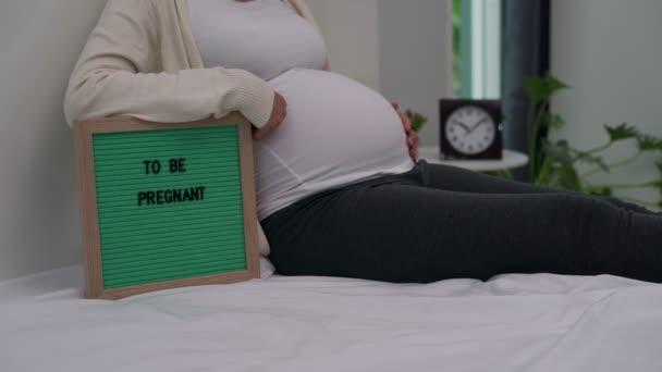 妊婦は緑の板で 妊娠することを 女性は妊娠を示すソーシャルメディアに写真や投稿を投稿する準備をしています — ストック動画