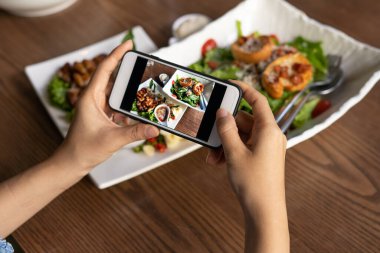 Kadın eli restorandaki yemek masasında yemek fotoğrafı çekmek için bir cep telefonu kullanıyor. Cep telefonu kavramlı fotoğrafçılık