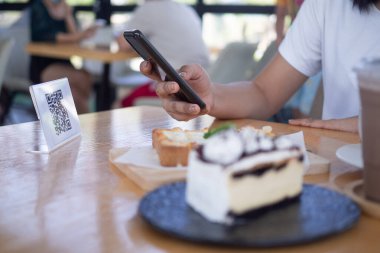 Kadınların elleri yemek menüsünü seçmek için QR kodunu tarıyor. İndirim için tarama yap ya da yiyecek için ödeme yap. Para transferi için telefon kullanma ya da nakit olmadan internet üzerinden para ödeme kavramı..