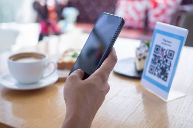Kadınların elleri yemek menüsünü seçmek için QR kodunu tarıyor. İndirim için tarama yap ya da yiyecek için ödeme yap. Para transferi için telefon kullanma ya da nakit olmadan internet üzerinden para ödeme kavramı..