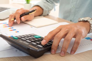 İşadamı, ofisteki masasındaki mali rapordaki rakamları hesaplamak için hesap makinesi kullanıyor. Hesap makinesi konsepti, işletme finans muhasebesi