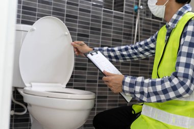 Male engineer inspects the installation of sanitary ware in the bathroom. Inspectors check job details before delivering to customers.
