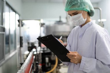 Bir teknoloji uzmanı ya da müfettiş yiyecek fabrikası üretim hattının siparişlerini doğrulamak için panoya not alıyor. Üretim kontrol çalışanları