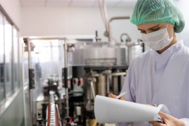 Bir teknoloji uzmanı ya da müfettiş yiyecek fabrikası üretim hattının siparişlerini doğrulamak için panoya not alıyor. Üretim kontrol çalışanları