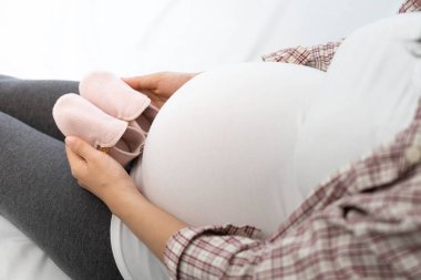 8 aylık hamile bir kadın bebek için ayakkabı hazırlamaktan mutluluk duyar. İyi bir anne ya da anne