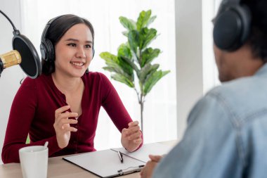 Asyalı radyo sunucusu Podcast stüdyoda. Bir erkek ve kadın konuşmacı internet üzerinden ev izleyicisiyle canlı olarak konuşuyor.