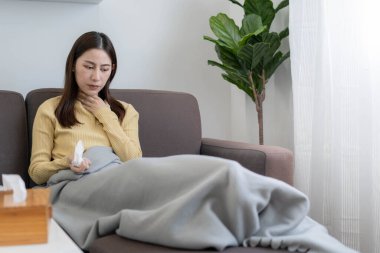 Hasta Asyalı kadın evde kanepede yatıyor. Baş ağrısı, soğuk algınlığı, öksürük ve ateşi var.. 