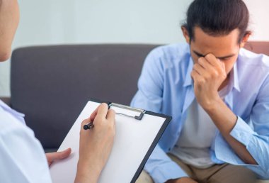 The psychologist talks to the mentally ill patient and takes a note to treatment. Asian men are stressed and frustrated with life problems. Psychologists talk to patients for treatment.