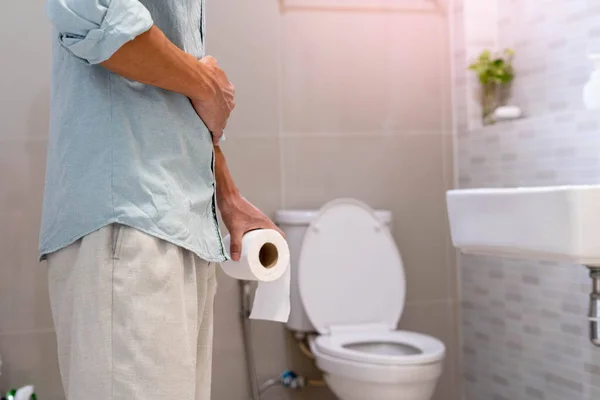 stock image Men are standing in front of the bathroom door using their hands to hold the abdomen with severe abdominal pain or diarrhea. The concept of stomach cramps, diarrhea