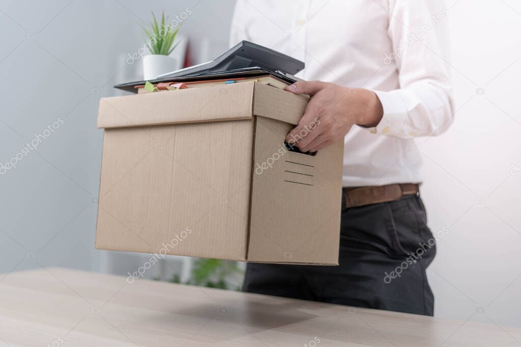 A businessman holds a box for personal items after sending a resignation letter to an executive or manager. Include information about resignation and vacancies and job changes.