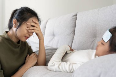 Stress woman take care of little ill daughter. Sick child lying on bed under blanket, with worried. single mom taking care of sick daughter at home. child has a high fever. covers on the couch and ill