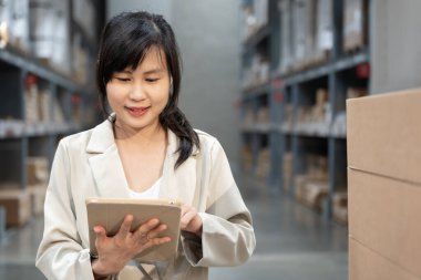 Asyalı kadın işyeri sahibi dijital tablet kullanıyor dağıtım deposu fabrikasındaki stok ürün envanterini kontrol ediyor. Lojistik iş gemisi ve teslimatı, envanter akışı, profesyonel iş akışı..