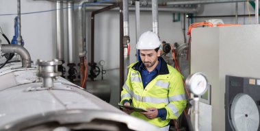 Güvenlik kaskı takan mühendisler veya fabrika yöneticileri üretim hattındaki makineleri inceler. Kamu müfettişi makineyi kontrol et ve standardı karşılamak için sistemi test et. makine, bakım.