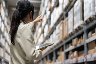 Asyalı kadın işyeri sahibi dijital tablet kullanıyor dağıtım deposu fabrikasındaki stok ürün envanterini kontrol ediyor. Lojistik iş gemisi ve teslimatı, envanter akışı, profesyonel iş akışı..