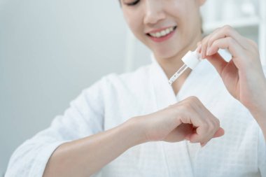 Güzel Asyalı kadın gülümsemesi ve iyi cilt için test serumu. Sağlıklı bir kadın yüzüne krem sürün ve makyaj yapın. Cilt kremi reklamı, kırışıklık önleyici, bebek yüzü, beyazlatma, nemlendirici.