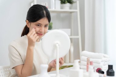 Güzel bir Asyalı kadın aynanın karşısına oturur ve makyaja gülümser. Makyaj yapan sağlıklı bir kadının yüzü. Reklam, yaşam tarzı, kozmetik, makyaj malzemeleri, güzellik etkinliği, güzellik uzmanı.