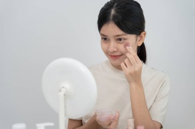 Güzel bir Asyalı kadın aynanın karşısına oturur ve makyaja gülümser. Makyaj yapan sağlıklı bir kadının yüzü. Reklam, yaşam tarzı, kozmetik, makyaj malzemeleri, güzellik etkinliği, güzellik uzmanı.