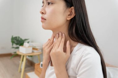 Asyalı kadın boğazı ağrıdığı için boynuna takıldı. Dişi bademcik iltihabı iltihaba neden olur. Su alarak, antibiyotik alarak, doktora, virüse, korona virüsüne, grip virüsüne danışarak,