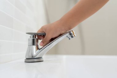 Little kid hand closed the faucet at sink in house with mom. Mother teaches child to save water. keeps turning off the water to save world energy and protect the environment, world water day