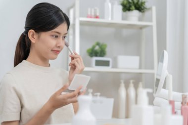 Güzel bir Asyalı kadın aynanın karşısına oturur ve makyaja gülümser. Makyaj yapan sağlıklı bir kadının yüzü. Reklam, yaşam tarzı, kozmetik, makyaj malzemeleri, güzellik etkinliği, güzellik uzmanı.