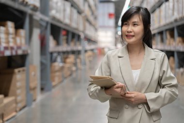 Asyalı kadın işyeri sahibi dijital tablet kullanıyor dağıtım deposu fabrikasındaki stok ürün envanterini kontrol ediyor. Lojistik iş gemisi ve teslimatı, envanter akışı, profesyonel iş akışı..