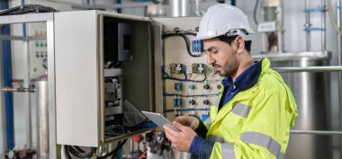 Güvenlik kaskı takan mühendisler veya fabrika yöneticileri üretim hattındaki makineleri inceler. Müfettiş standardı karşılamak için sistemi test etmek için makineyi açtı. makine bakımı