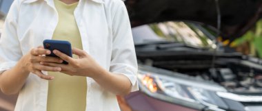 breakdown, broken car, repair. Woman uses mobile phone check insurance premiums through application due to car accident . Find garage to get car fixed during country tour, waiting for help, emergency