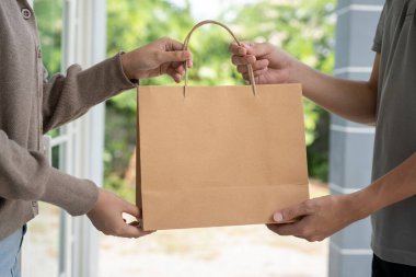 Mutlu gülümseyen Asyalı kadın, kurye evinden bir paket yiyecek alıyor. Teslimatçı ekspres teslimat gönderdi. Çevrimiçi alışveriş, kağıt konteynır, paket servisi, postacı, dağıtım servisi, paketler