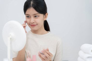 Güzel bir Asyalı kadın aynanın karşısına oturur ve makyaja gülümser. Makyaj yapan sağlıklı bir kadının yüzü. Reklam, yaşam tarzı, kozmetik, makyaj malzemeleri, güzellik aktiviteleri, güzellik