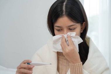 Young Asian woman having high fever while checking body temperature, female sneezing and runny nose with seasonal influenza, allergic, digital thermometer, virus, coronavirus, illness, respiratory