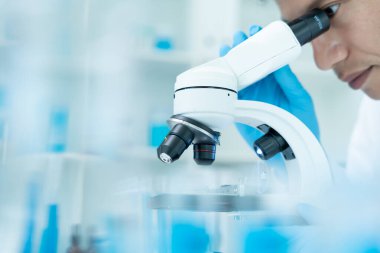 Bilimadamı ileri bilimsel laboratuvarda biyokimyasal örnekleri analiz ediyor. Tıbbi profesyonel kullanım mikroskobu virüsün mikrobiyolojik gelişimini gösteriyor. Fen laboratuvarında biyoteknoloji araştırması.