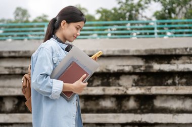 Sırt çantası ve kitapları açık havada olan Asyalı güzel bir öğrenci. Üniversite kampüsünde kitap taşımaktan mutlu gülümseyen kız. Uluslararası Asya Üniversitesi 'nde kadın portresi. Eğitim, eğitim, okul