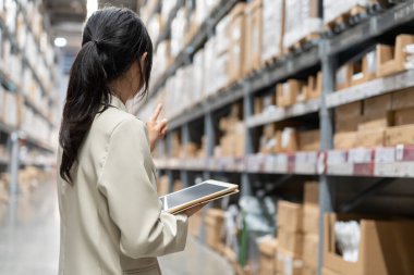 Asyalı kadın işyeri sahibi dijital tablet kullanıyor dağıtım deposu fabrikasındaki stok ürün envanterini kontrol ediyor. Lojistik iş gemisi ve teslimatı, envanter akışı, profesyonel iş akışı..