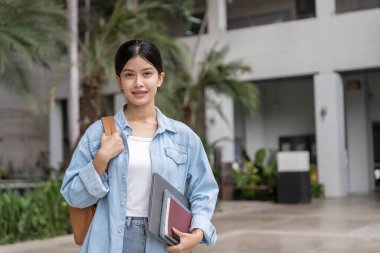 Sırt çantası ve kitapları açık havada olan Asyalı güzel bir öğrenci. Üniversite kampüsünde kitap taşımaktan mutlu gülümseyen kız. Uluslararası Asya Üniversitesi 'nde kadın portresi. Eğitim, eğitim, okul