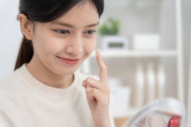 Güzel Asyalı kadın gülümsüyor, cilt kremi kullanıyor. Sağlıklı bir kadın yüzüne krem sürün ve makyaj yapın. Cilt kremi reklamı, kırışıklık önleyici, bebek yüzü, beyazlatma, nemlendirici, gözenekleri sıkılaştırma serumu.