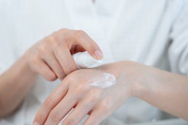 Güzel Asyalı kadın cilt kremini kontrol ediyor. Sağlıklı bir kadın yüzüne krem sürün ve makyaj yapın. Cilt kremi reklamı, kırışıklık önleyici, bebek yüzü, beyazlatma, nemlendirici.