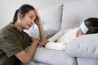 Stress woman take care of little ill daughter. Sick child lying on bed under blanket, with worried. single mom taking care of sick daughter at home. child has a high fever. covers on the couch and ill