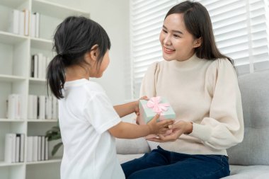 Asyalı kız çocukları güzel anneleri için arkalarında hediye kutuları saklarken anne evde kanepede oturuyor. Evde özel bir kutlama yapıyoruz, mutlu yıllar.