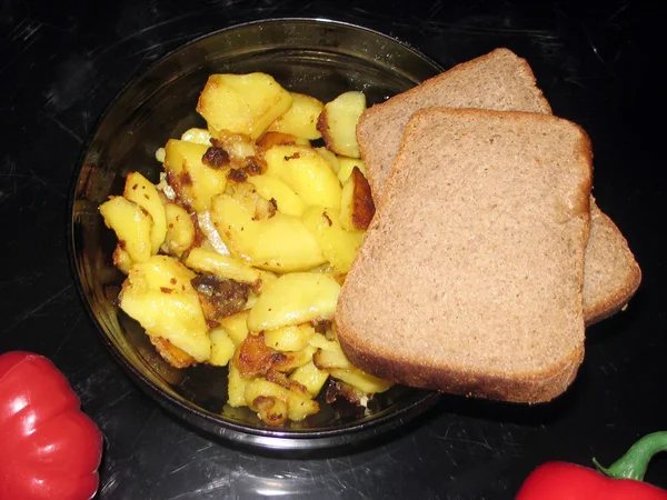 Gebakken aardappelen, zwarte brood op een zwarte achtergrond — Stockfoto