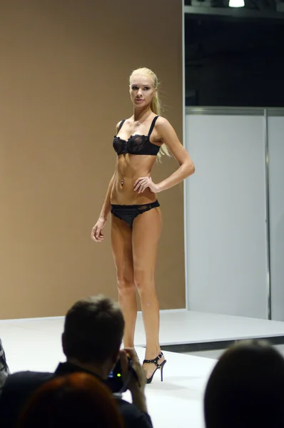 5e internationale tentoonstelling van ondergoed, beachwear, huis sportkleding en breigoed Lingrie Expo Moskou Aututumn September jonge blonde vrouw in zwarte ondergoed kijken spectaculaire ommekeer — Stockfoto